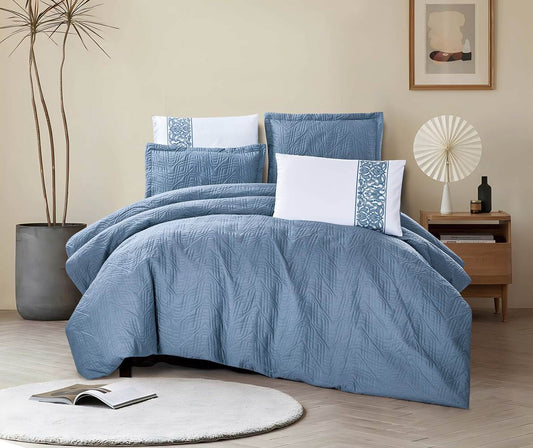 A navy geometric comforter set on a bed, with additional pillows placed against the headboard, presented in a room setting with decorative items and a book on the foreground floor.