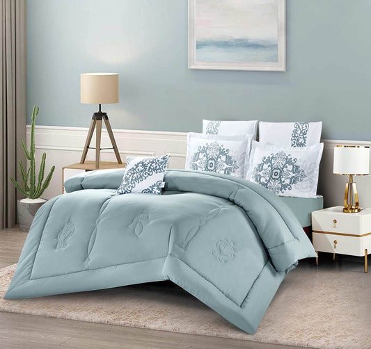 A bedding set with a floral and geometric pattern in blue and white colors, displayed on a bed with a nightstand and lamp in the background.