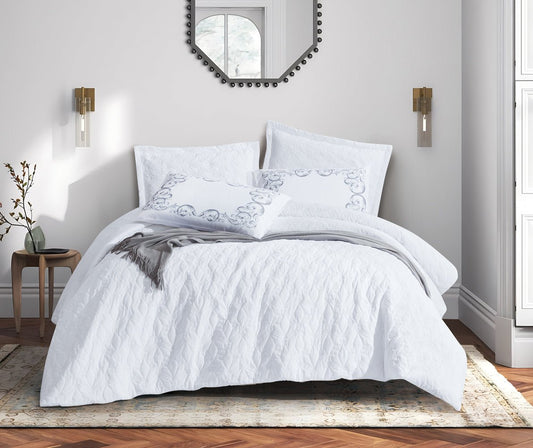 A white bedding set with floral patterns displayed on a bed in a bedroom setting with decorative pillows, bed sheets, and a duvet cover.