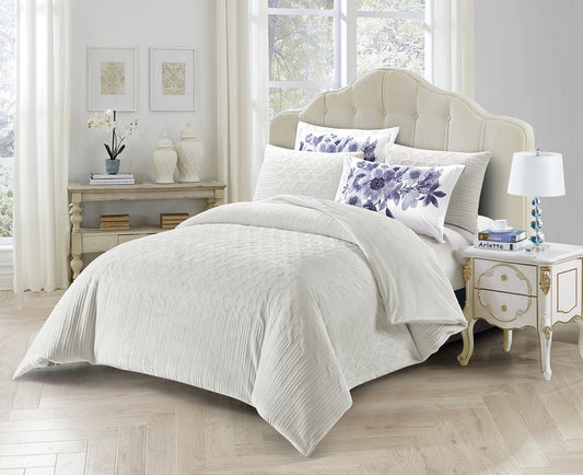 A king-size bedding set displayed on a bed, featuring a quilted design with floral embroidery detail, along with two velvet pillow shams with a matching design.