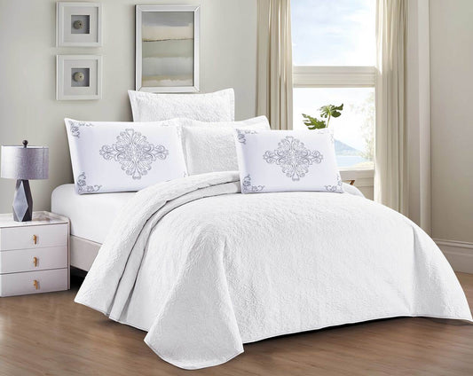 A white floral summer comforter set displayed on a bed, with a matching white curtain and a nightstand with a lamp in the background.