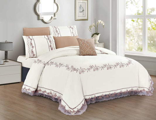 A bedding set with floral applique design, displayed on a bed in a room with beige walls and a window. The set includes a comforter, pillows, and a bedsheet.
