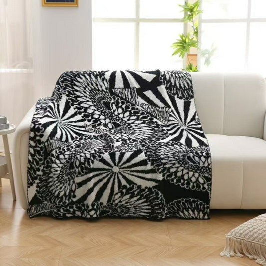 A black and white geometric patterned blanket draped over the back of a sofa in a room with wooden flooring and a window.