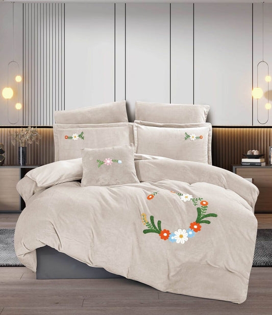 A beige floral embroidered comforter set on a king-sized bed, with two decorative pillows, in a room with a wooden headboard and lights on the wall.