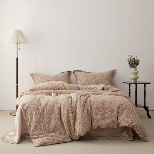 A beige luxury jacquard duvet cover set on a bed, with a lamp and a vase with flowers on the side table.