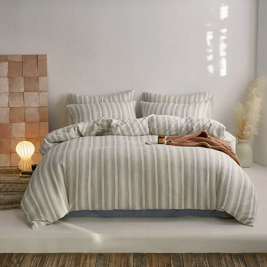 A striped cotton duvet cover set displayed on a bed in a bedroom setting with a lamp and decorative items in the background.