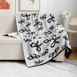 A gray and black knit throw blanket with bow patterns, draped over the arm of a beige sofa.