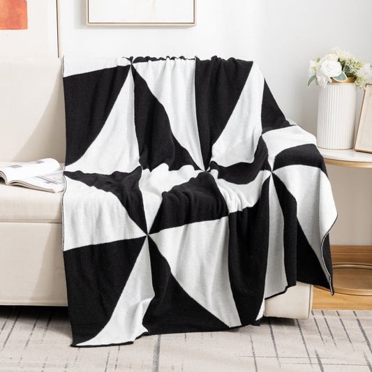 A black and white geometric patterned blanket draped over a couch with a white vase and flowers on the side table.