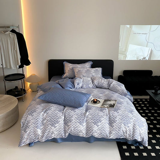 A duvet cover set with a geometric pattern, displayed on a bed in a room with a minimalist decor. The set includes matching pillows and a tote bag.