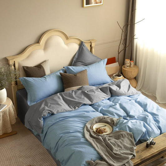 A bed with a blue and gray reversible bedding set, including a comforter, sheets, and pillows, in a bedroom setting with decorative items.