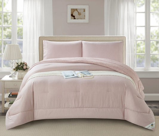 A blush pink minimalist quilted comforter set on a bed in a room with a window and lamp in the background.