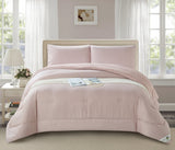 A blush pink minimalist quilted comforter set on a bed in a room with a window and lamp in the background.