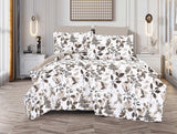 A bed with a white spread featuring a green and brown leaf print, displayed in a room with decorative lighting and a framed picture on the wall.