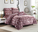 A burgundy lace quilted comforter set with pom-pom trim displayed in a bedroom setting, including a comforter, pillowcases, and a bedsheet.