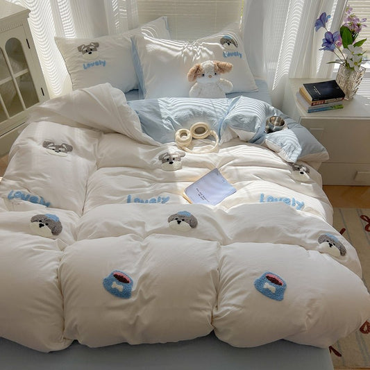 A white bedding set with cute animal applique designs on a bed, with a blue and a white pillow, a comforter, and a duvet cover.