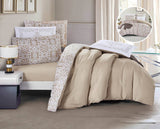 A beige and floral comforter set on a bed, with a pillow featuring a beige solid color on one side and a floral pattern on the other, displayed in a well-lit room with curtains and a book on the bed.