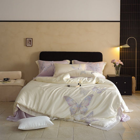 A bedroom set with a beige bedsheet featuring purple butterfly embroidery, accompanied by matching pillows and a duvet cover.