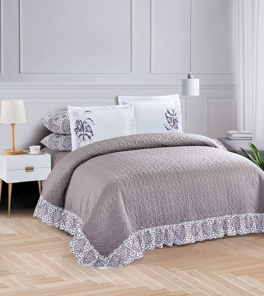 A gray bed spread with a floral trim on the edges, displayed on a bed with matching pillows.