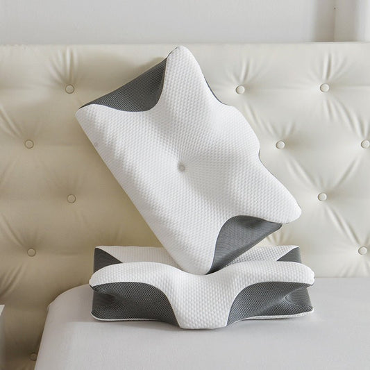 A butterfly-shaped cervical comfort pillow, with gray and white colors, displayed on a bed.