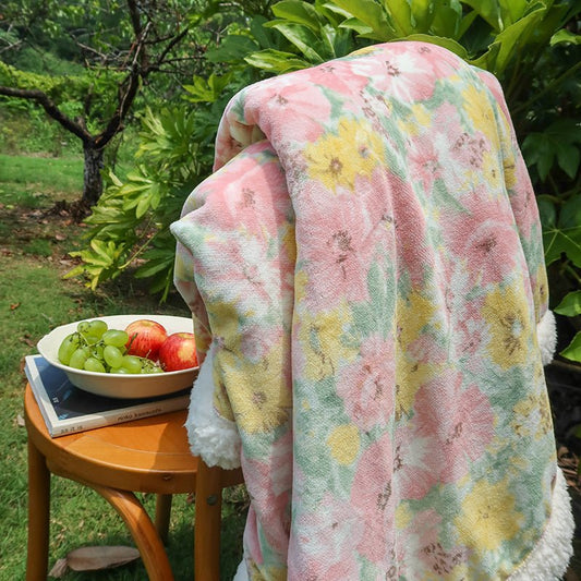 A person is lying on a wooden daybed under a multicolored floral blanket with a bowl of fruits placed next to them.