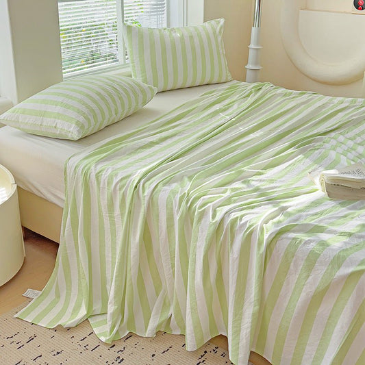 A green and white striped sheet on a bed, with a pillowcases matching the pattern.