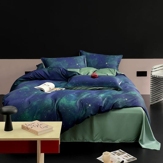 A bedding set with a galaxy print, featuring a starry night sky pattern in blue and green colors, displayed on a bed with other bedding items and a book on a bedside table.