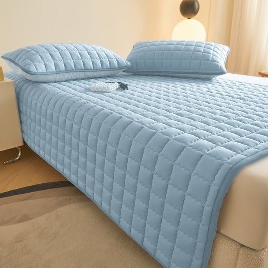 A blue quilted mattress protector on a bed with two pillows, displayed in a bedroom setting.