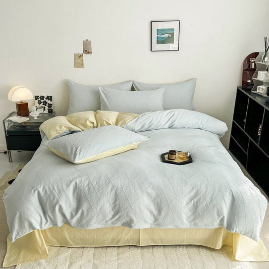 A bedroom with a bed dressed in a blue and white 3D textured cotton duvet cover set, accompanied by matching pillows and a bed skirt, with a side table and lamp.