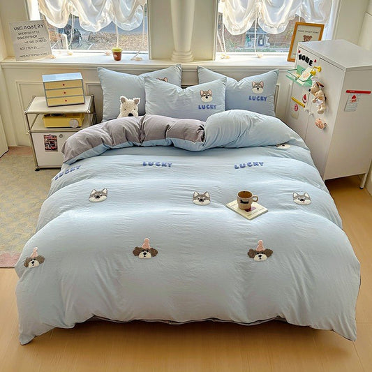 A blue duvet cover set with puppy appliqué designs displayed on a bed, accompanied by a pillow or two and a comforter, in a room setting with a window and furniture in the background.