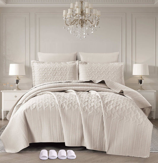 A cream-colored bedding set displayed on a bed, with a pattern that resembles waves. The room has a luxurious decor with a chandelier, lamps, and a pair of slippers at the foot of the bed.