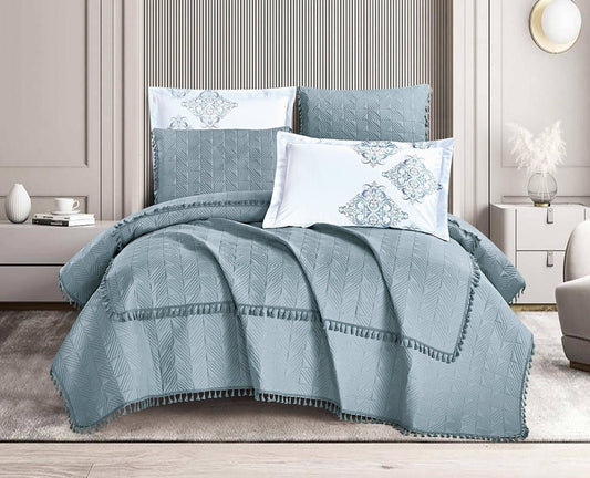 A navy blue quilt with tassel detailing, displayed on a bed in a room with light decor. The quilt set includes matching pillows.