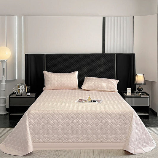 A beige, quilted fitted sheet on a bed with rounded corners, displayed in a bedroom setting with pillows and a bedhead in the background.