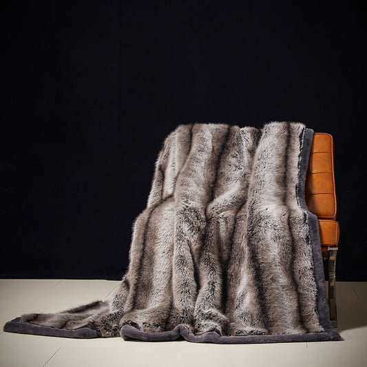 A luxury blanket with a fur-like texture draped over the back of a wooden chair, displayed in a dimly lit room.