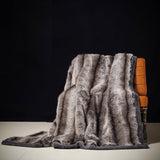 A luxury blanket with a fur-like texture draped over the back of a wooden chair, displayed in a dimly lit room.