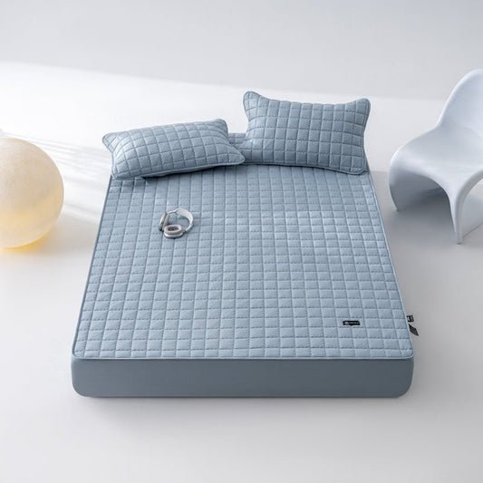 A gray hospital grade waterproof sheet on a bed, with two matching pillows, presented in a bright room setting.