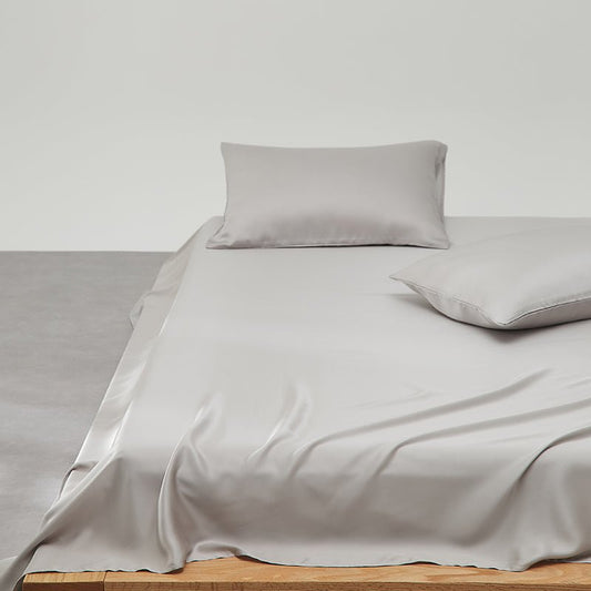 A gray Tencel sateen sheet set on a bed, with a pillow and a pillowcase, against a white background.
