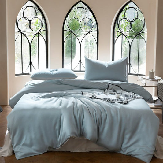 A blue Tencel bedding set on a bed with pillows, placed in a room with large windows and decorative grills.