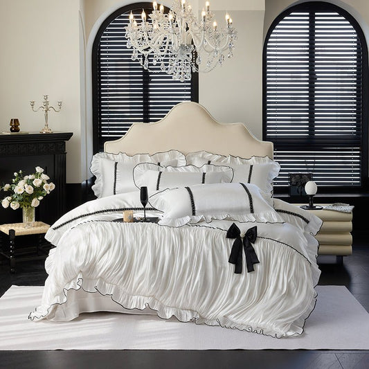 A luxurious white Tencel duvet cover set on a bed, with decorative black bows and ruffled details, displayed in an elegantly decorated bedroom setting.