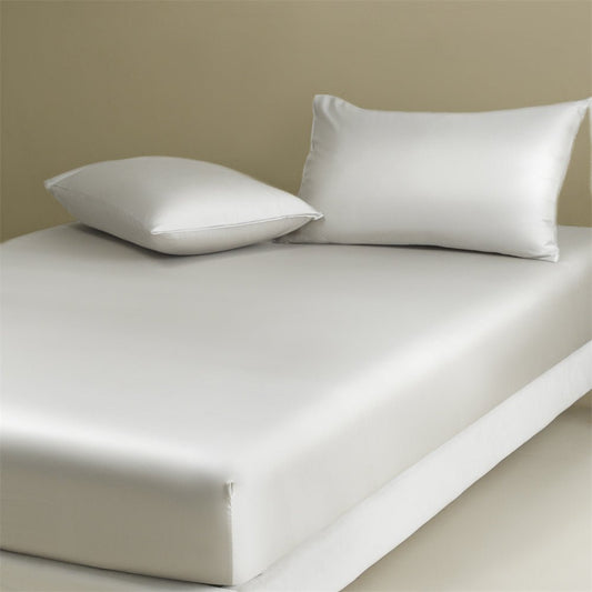 A white fitted sheet on a bed with two white pillows on top. The image showcases a neat and tidy bed with a fitted sheet.