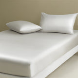 A white fitted sheet on a bed with two white pillows on top. The image showcases a neat and tidy bed with a fitted sheet.