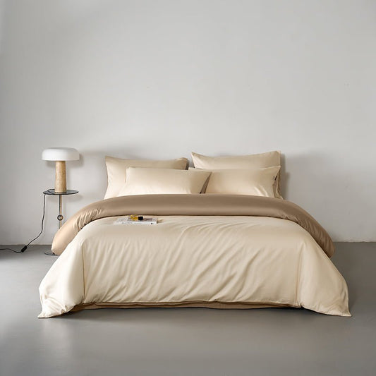 A beige minimalist solid cotton duvet cover set on a bed, with a lamp and a book on the side table.