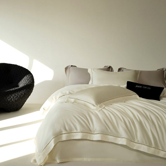 A white duvet cover and pillowcases set on a bed, with a black decorative object on the side table and a window allowing natural light to enter the room.