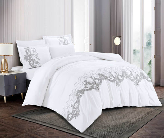 A white bedding set with embroidered patchwork design, displayed on a bed with accompanying pillows and a quilt cover.