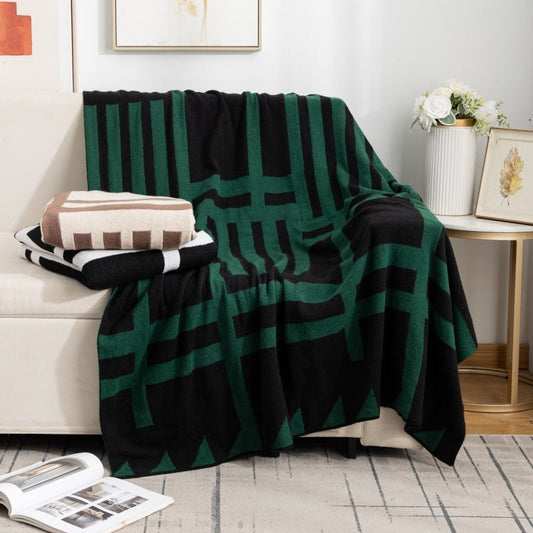 A green and black striped blanket thrown over the back of a sofa with a remote control and a magazine on the foreground.
