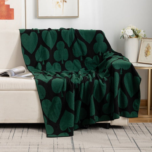 A green geometric patterned blanket thrown over the back of a beige sofa in a living room setting.