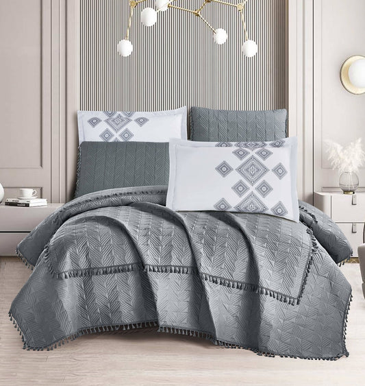 A Mist Grey Tassel Spread Set on a bed, with matching pillows and a textured grey quilt, in a room with a modern decor.