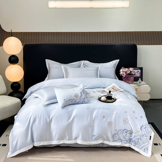 A blue duvet cover set with white and blue embroidery on a double bed, displayed in a bedroom setting with decorative pillows, bed sheets, and a quilt.