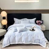 A blue duvet cover set with white and blue embroidery on a double bed, displayed in a bedroom setting with decorative pillows, bed sheets, and a quilt.