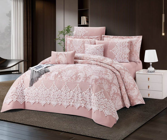 A blush pink lace comforter set on a bed, with additional pillows and bed decor in a matching color scheme, set against a bedroom backdrop.