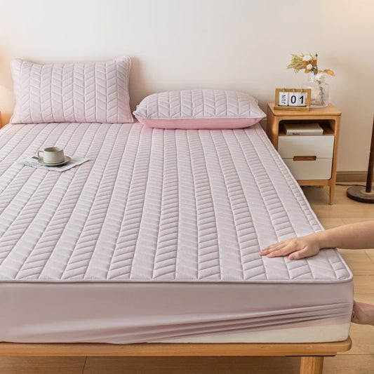 A pink fitted sheet on a bed, with a person's hand adjusting it. A pillow, a cup, and a wooden nightstand are also visible in the room.